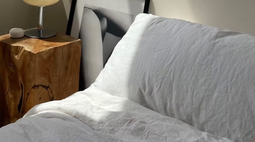 Cama blanca junto a una mesita de madera, iluminada por luz natural